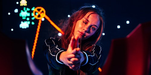 A woman with her fingers in the shape of a gun infront of gaming-style neon signs