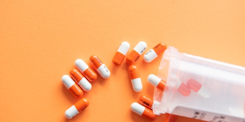 A pot of pills spilled over an orange surface