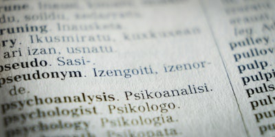 A close-up photograph of a page in the dictionary focuses on the word 'pseudonym'