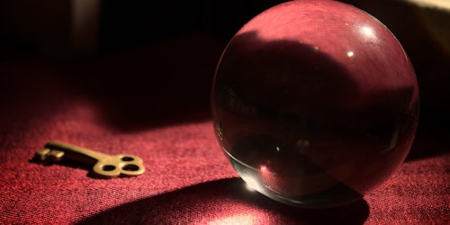 Crystal ball next to gold key on red table cloth