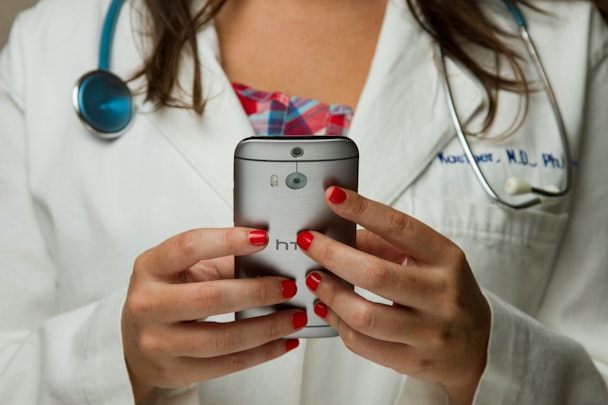 A doctor wearing a stethoscope uses a handheld device